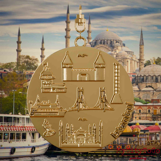 Halskette mit Drehwirbel und Vorderseite eines vergoldeten Schmuckanhängers, auf dem Reliefs bekannter Sehenswürdigkeiten der Stadt Istanbul abgebildet sind. Den Hintergrund bildet eine Ansicht der Stadt Istanbul.
