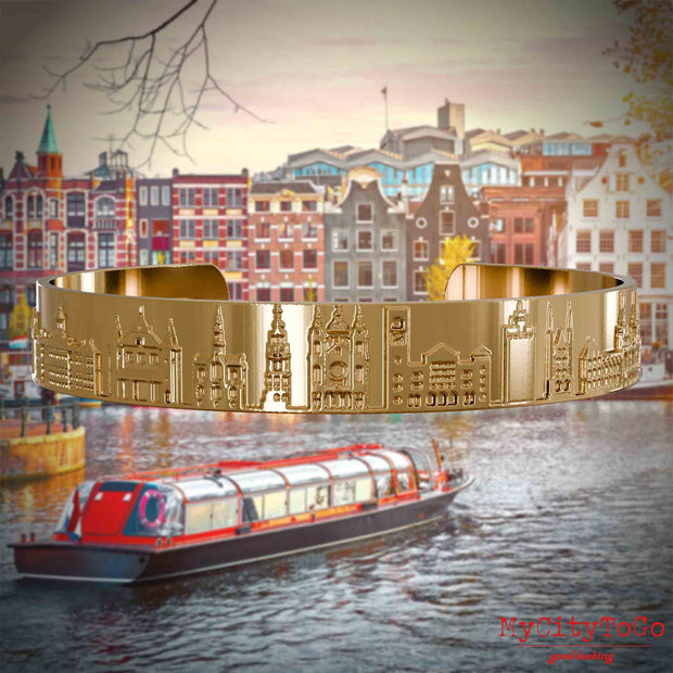 Vergoldeter Armreif mit Reliefs bekannter Sehenswürdigkeiten der Stadt Amsterdam. Den Hintergrund bildet eine Ansicht der Stadt Amsterdam.