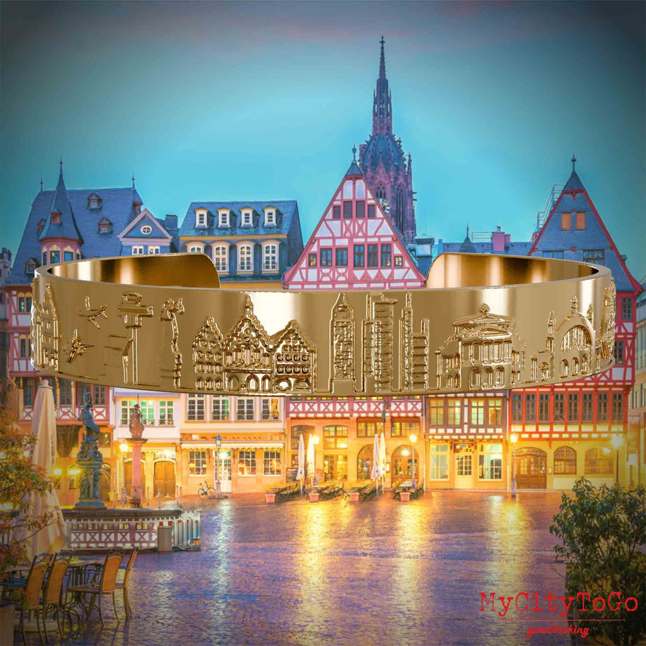Vergoldeter Armreif mit Reliefs bekannter Sehenswürdigkeiten der Stadt Frankfurt. Den Hintergrund bildet eine Ansicht der Stadt Frankfurt.
