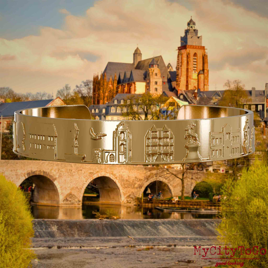 Vergoldeter Armreif mit Reliefs bekannter Sehenswürdigkeiten der Stadt Wetzlar. Den Hintergrund bildet eine Ansicht der Stadt Wetzlar.