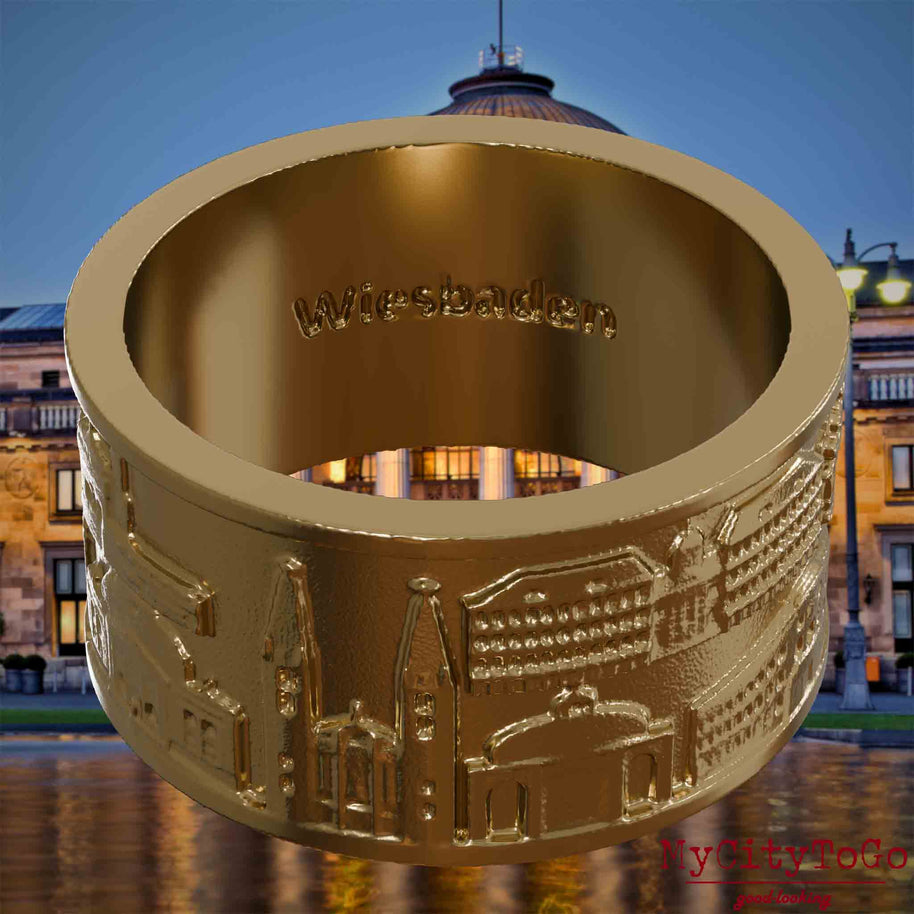 Ring aus vergoldetem Edelstahl mit Reliefs bekannter Sehenswürdigkeiten der Stadt Wiesbaden und einer Gravur des Stadtnamens auf der Innenseite. Den Hintergrund bildet eine Ansicht der Stadt Wiesbaden.
