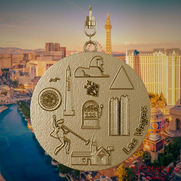 Halskette mit Drehwirbel und Vorderseite eines Schmuckanhängers aus vergoldetem Edelstahl, auf dem Reliefs bekannter Sehenswürdigkeiten der Stadt Las Vegas abgebildet sind. Den Hintergrund bildet eine Ansicht der Stadt Las Vegas.

