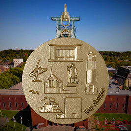 Halskette mit Drehwirbel und Rückseite eines Schmuckanhängers aus vergoldetem Edelstahl, auf dem Reliefs bekannter Sehenswürdigkeiten der Stadt Bochum abgebildet sind. Den Hintergrund bildet eine Ansicht der Stadt Bochum .
