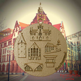Halskette mit Drehwirbel und Rückseite eines Schmuckanhängers aus vergoldetem Edelstahl, auf dem Reliefs bekannter Sehenswürdigkeiten der Stadt Dortmund abgebildet sind. Den Hintergrund bildet eine Ansicht der Stadt Dortmund.