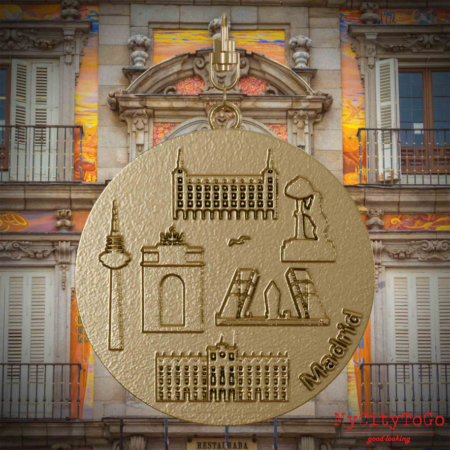 Halskette mit Drehwirbel und Vorderseite eines Schmuckanhängers aus vergoldetem Edelstahl, auf dem Reliefs bekannter Sehenswürdigkeiten der Stadt Madrid abgebildet sind. Den Hintergrund bildet eine Ansicht der Stadt Madrid.
