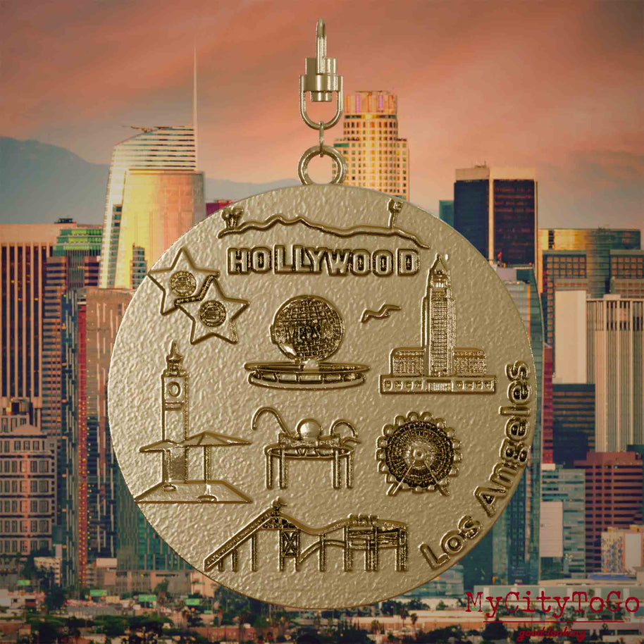 Halskette mit Drehwirbel und Vorderseite eines Schmuckanhängers aus vergoldetem Edelstahl, auf dem Reliefs bekannter Sehenswürdigkeiten der Stadt Los Angeles abgebildet sind. Den Hintergrund bildet eine Ansicht der Stadt Los Angeles.
