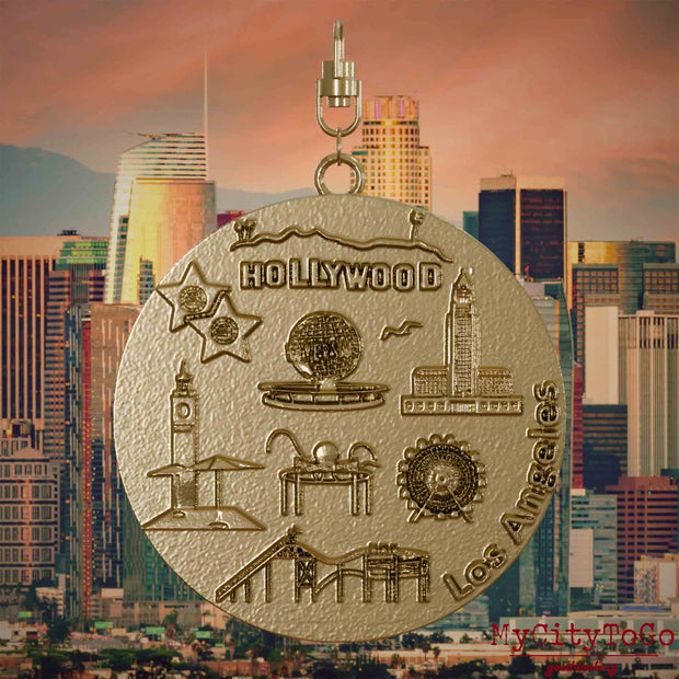 Halskette mit Drehwirbel und Vorderseite eines Schmuckanhängers aus vergoldetem Edelstahl, auf dem Reliefs bekannter Sehenswürdigkeiten der Stadt Los Angeles abgebildet sind. Den Hintergrund bildet eine Ansicht der Stadt Los Angeles.
