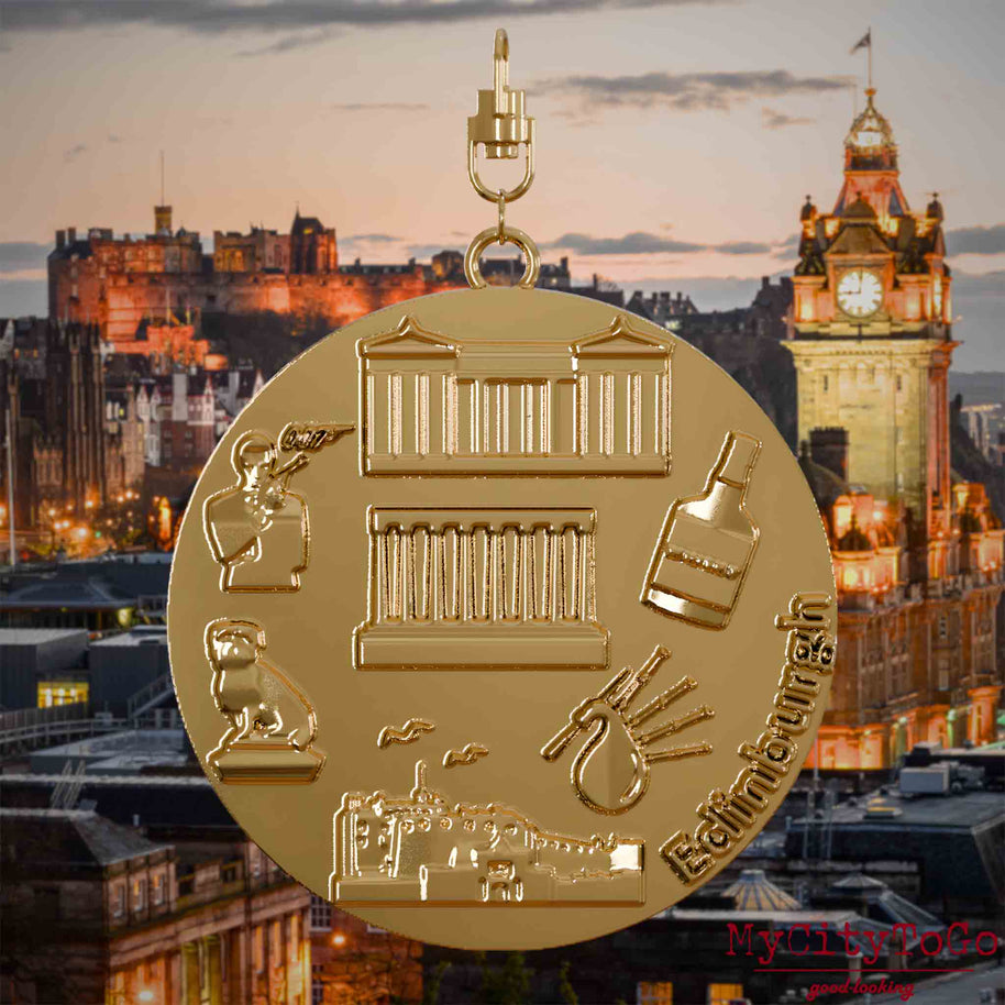 Halskette mit Drehwirbel und Vorderseite eines vergoldeten Schmuckanhängers, auf dem Reliefs bekannter Sehenswürdigkeiten der Stadt Edinburgh abgebildet sind. Den Hintergrund bildet eine Ansicht der Stadt Edinburgh.
