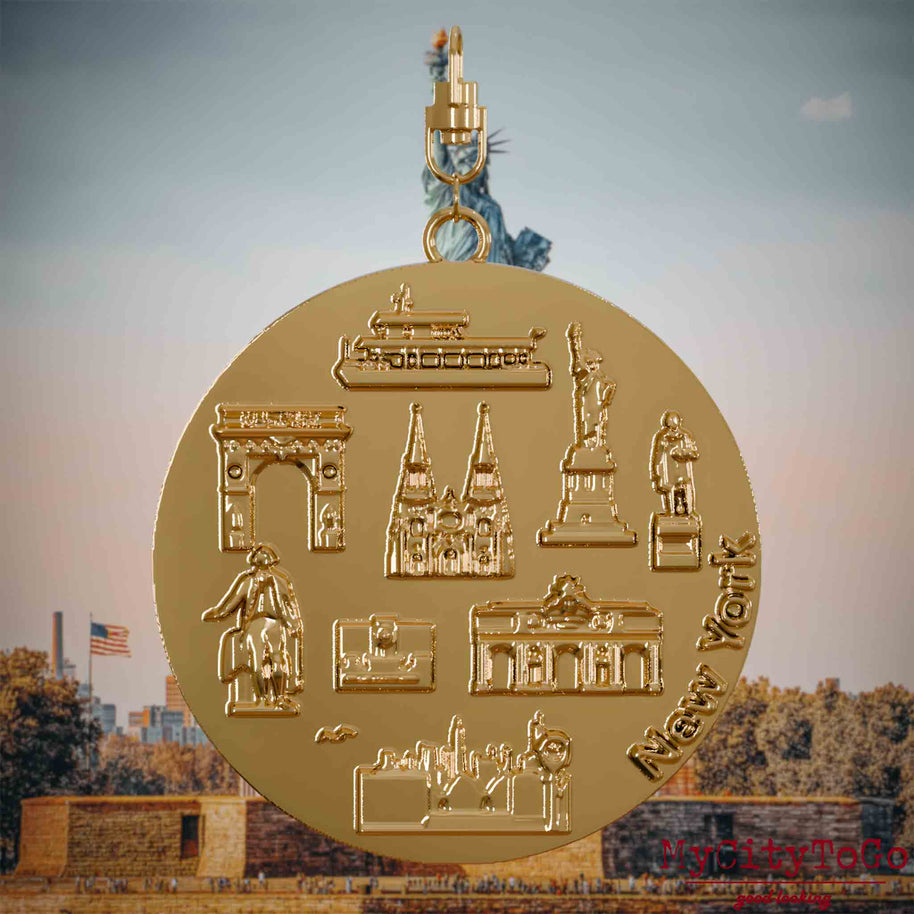 Halskette mit Drehwirbel und Vorderseite eines vergoldeten Schmuckanhängers, auf dem Reliefs bekannter Sehenswürdigkeiten der Stadt New York abgebildet sind. Den Hintergrund bildet eine Ansicht der Stadt New York.
