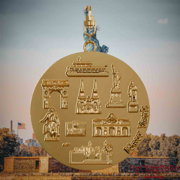 Halskette mit Drehwirbel und Vorderseite eines vergoldeten Schmuckanhängers, auf dem Reliefs bekannter Sehenswürdigkeiten der Stadt New York abgebildet sind. Den Hintergrund bildet eine Ansicht der Stadt New York.
