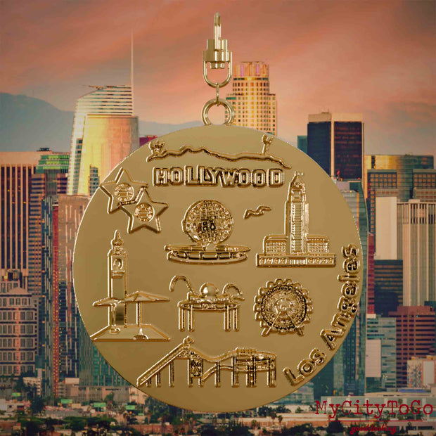 Halskette mit Drehwirbel und Vorderseite eines vergoldeten Schmuckanhängers, auf dem Reliefs bekannter Sehenswürdigkeiten der Stadt Los Angeles abgebildet sind. Den Hintergrund bildet eine Ansicht der Stadt Los Angeles.
