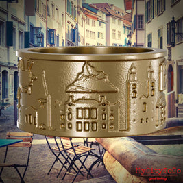 Ring aus vergoldetem Edelstahl mit Reliefs bekannter Sehenswürdigkeiten der Stadt Zuerich. Den Hintergrund bildet eine Ansicht der Stadt Zuerich.