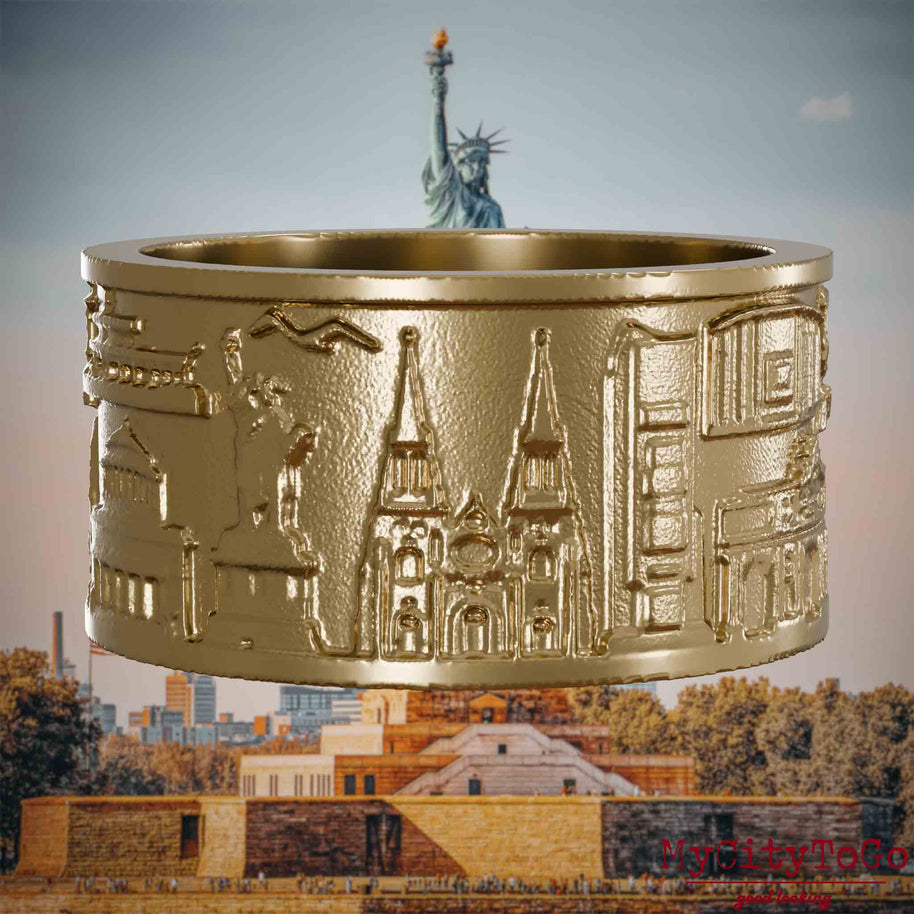 Ring aus vergoldetem Edelstahl mit Reliefs bekannter Sehenswürdigkeiten der Stadt New York. Den Hintergrund bildet eine Ansicht der Stadt New York.