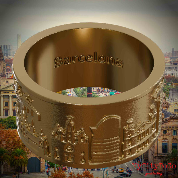 Ring aus vergoldetem Edelstahl mit Reliefs bekannter Sehenswürdigkeiten der Stadt Barcelona und einer Gravur des Stadtnamens auf der Innenseite. Den Hintergrund bildet eine Ansicht der Stadt Barcelona.