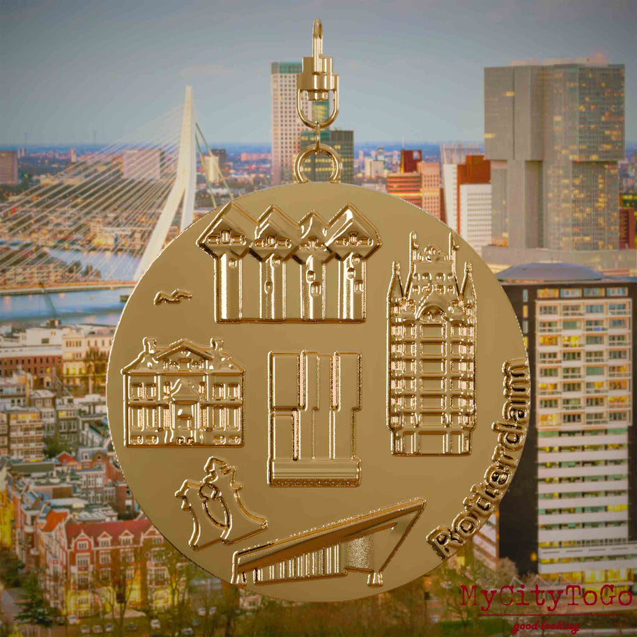 Halskette mit Drehwirbel und Vorderseite eines vergoldeten Schmuckanhängers, auf dem Reliefs bekannter Sehenswürdigkeiten der Stadt Rotterdam abgebildet sind. Den Hintergrund bildet eine Ansicht der Stadt Rotterdam.
