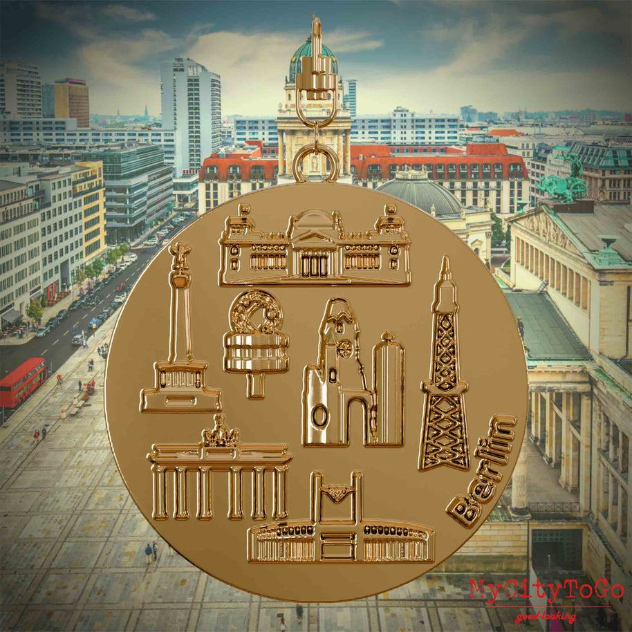 Halskette mit Drehwirbel und Rückseite eines vergoldeten Schmuckanhängers, auf dem Reliefs bekannter Sehenswürdigkeiten der Stadt Berlin abgebildet sind. Den Hintergrund bildet eine Ansicht der Stadt Berlin.