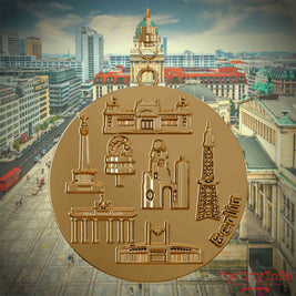 Halskette mit Drehwirbel und Rückseite eines vergoldeten Schmuckanhängers, auf dem Reliefs bekannter Sehenswürdigkeiten der Stadt Berlin abgebildet sind. Den Hintergrund bildet eine Ansicht der Stadt Berlin.