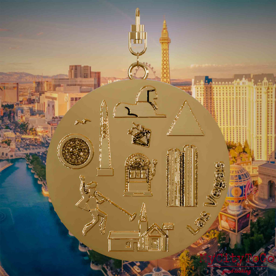 Halskette mit Drehwirbel und Vorderseite eines vergoldeten Schmuckanhängers, auf dem Reliefs bekannter Sehenswürdigkeiten der Stadt Las Vegas abgebildet sind. Den Hintergrund bildet eine Ansicht der Stadt Las Vegas.
