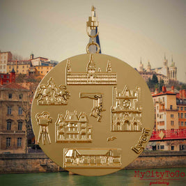 Halskette mit Drehwirbel und Vorderseite eines vergoldeten Schmuckanhängers, auf dem Reliefs bekannter Sehenswürdigkeiten der Stadt Lyon abgebildet sind. Den Hintergrund bildet eine Ansicht der Stadt Lyon.
