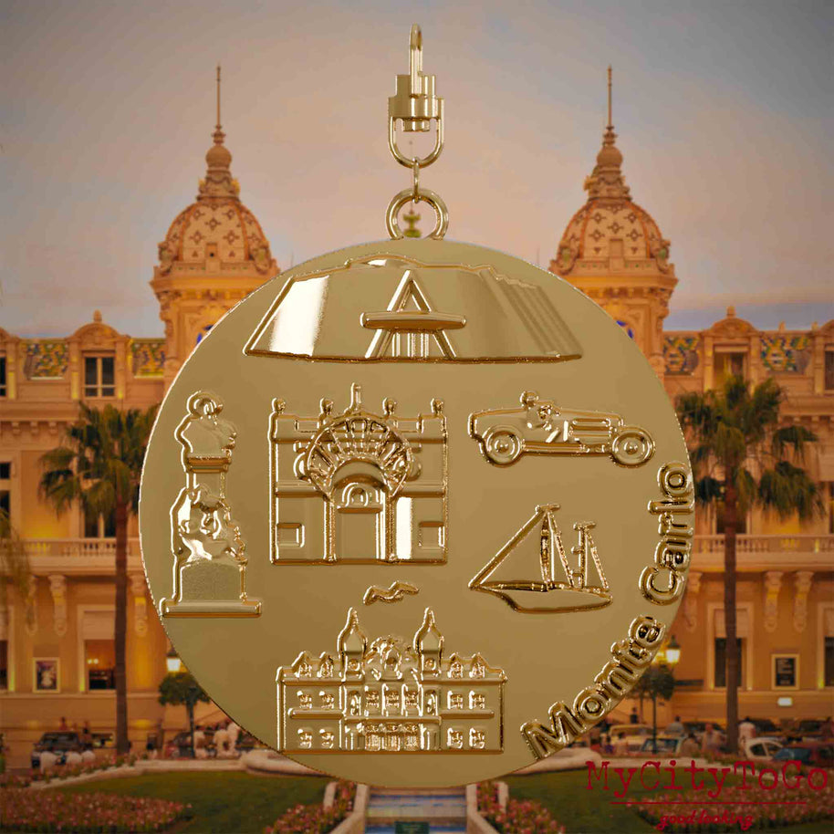 Halskette mit Drehwirbel und Vorderseite eines vergoldeten Schmuckanhängers, auf dem Reliefs bekannter Sehenswürdigkeiten der Stadt Monte Carlo abgebildet sind. Den Hintergrund bildet eine Ansicht der Stadt Monte Carlo.
