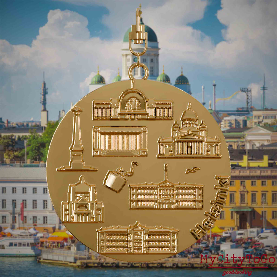 Halskette mit Drehwirbel und Vorderseite eines vergoldeten Schmuckanhängers, auf dem Reliefs bekannter Sehenswürdigkeiten der Stadt Helsinki abgebildet sind. Den Hintergrund bildet eine Ansicht der Stadt Helsinki.
