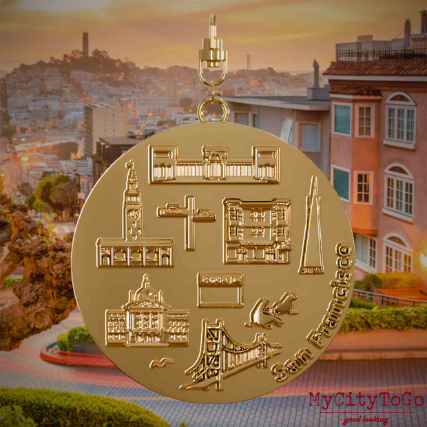 Halskette mit Drehwirbel und Vorderseite eines vergoldeten Schmuckanhängers, auf dem Reliefs bekannter Sehenswürdigkeiten der Stadt San Francisco abgebildet sind. Den Hintergrund bildet eine Ansicht der Stadt San Francisco.

