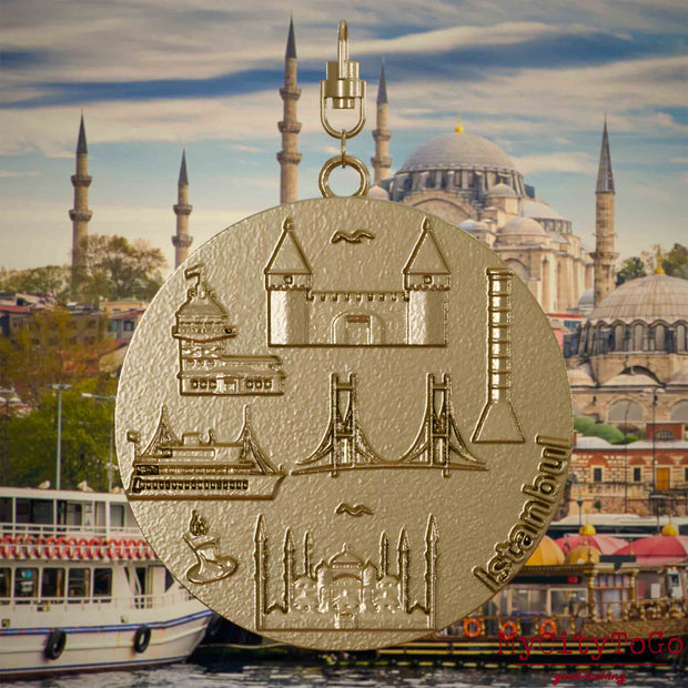Halskette mit Drehwirbel und Vorderseite eines Schmuckanhängers aus vergoldetem Edelstahl, auf dem Reliefs bekannter Sehenswürdigkeiten der Stadt Istanbul abgebildet sind. Den Hintergrund bildet eine Ansicht der Stadt Istanbul.

