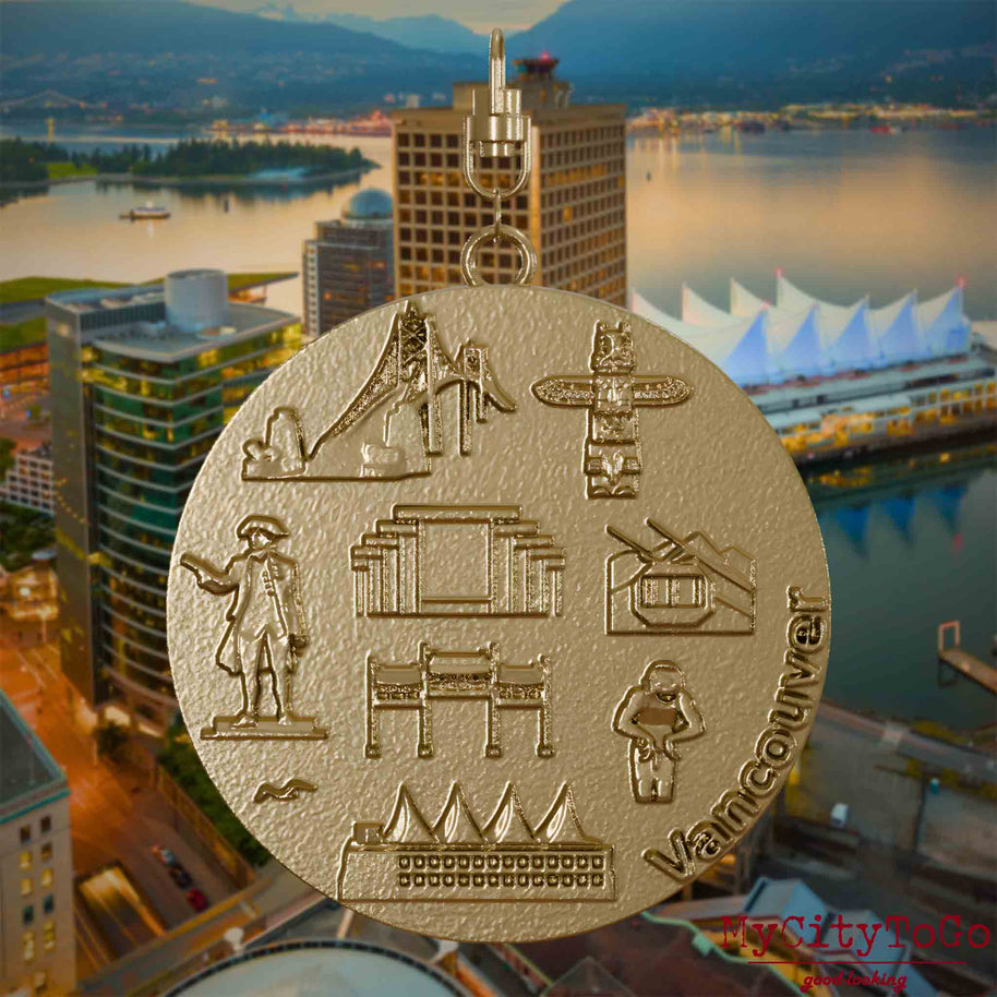 Halskette mit Drehwirbel und Vorderseite eines Schmuckanhängers aus vergoldetem Edelstahl, auf dem Reliefs bekannter Sehenswürdigkeiten der Stadt Vancouver abgebildet sind. Den Hintergrund bildet eine Ansicht der Stadt Vancouver.
