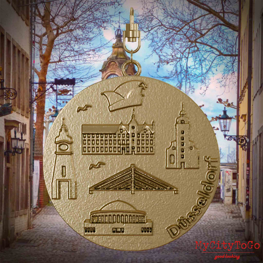 Halskette mit Drehwirbel und Rückseite eines Schmuckanhängers aus vergoldetem Edelstahl, auf dem Reliefs bekannter Sehenswürdigkeiten der Stadt Dusseldorf abgebildet sind. Den Hintergrund bildet eine Ansicht der Stadt Duesseldorf.