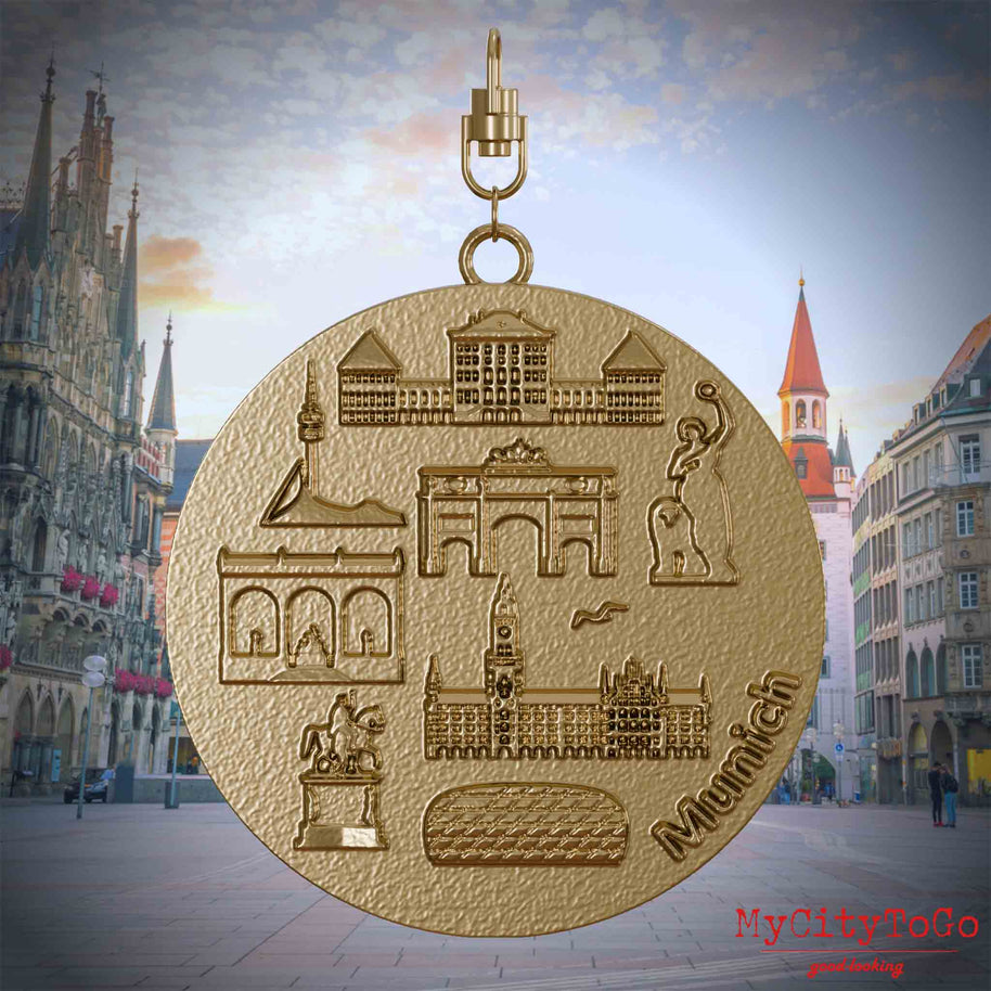 Halskette mit Drehwirbel und Rückseite eines Schmuckanhängers aus vergoldetem Edelstahl, auf dem Reliefs bekannter Sehenswürdigkeiten der Stadt Muenchen abgebildet sind. Den Hintergrund bildet eine Ansicht der Stadt Muenchen.