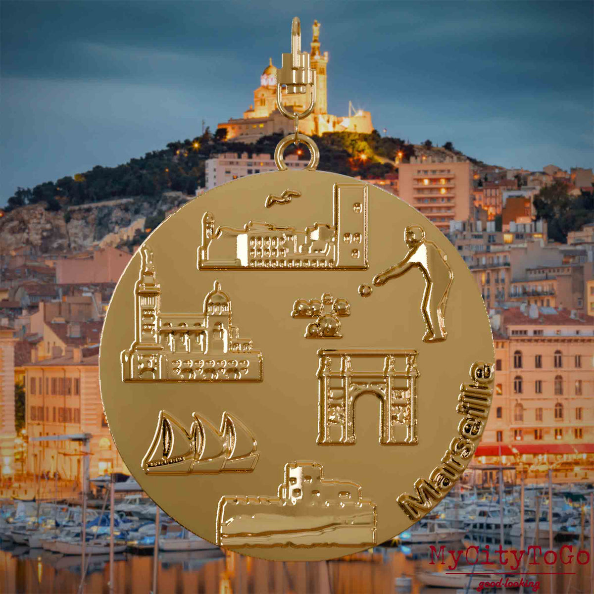 Halskette mit Drehwirbel und Vorderseite eines vergoldeten Schmuckanhängers, auf dem Reliefs bekannter Sehenswürdigkeiten der Stadt Marseille abgebildet sind. Den Hintergrund bildet eine Ansicht der Stadt Marseille.
