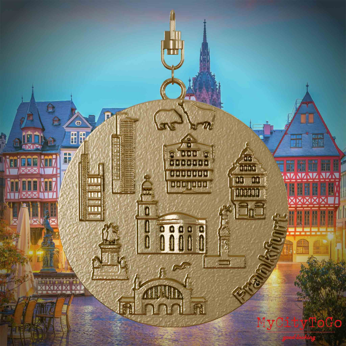 Halskette mit Drehwirbel und Vorderseite eines Schmuckanhängers aus vergoldetem Edelstahl, auf dem Reliefs bekannter Sehenswürdigkeiten der Stadt Frankfurt abgebildet sind. Den Hintergrund bildet eine Ansicht der Stadt Frankfurt.
