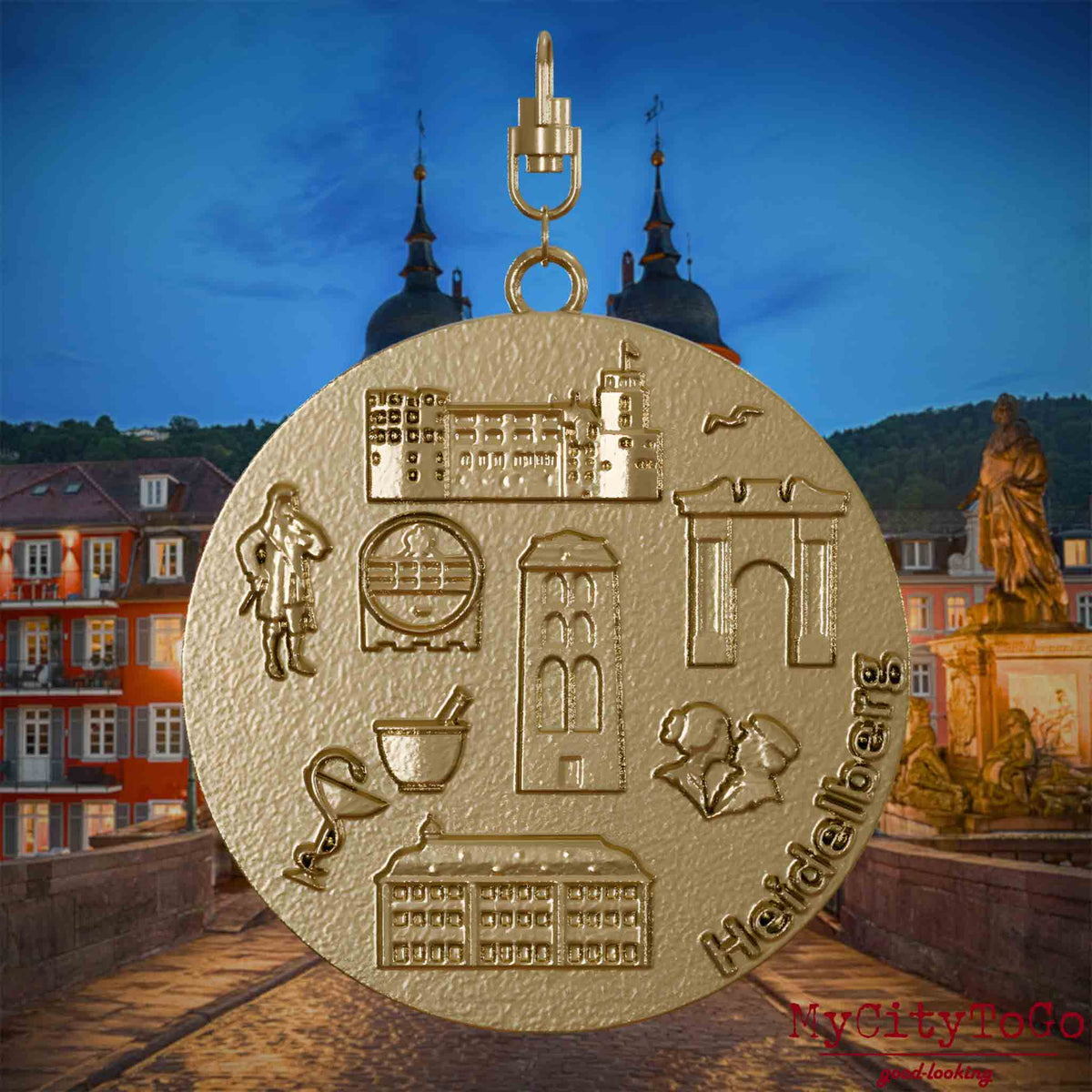 Halskette mit Drehwirbel und Vorderseite eines Schmuckanhängers aus vergoldetem Edelstahl, auf dem Reliefs bekannter Sehenswürdigkeiten der Stadt Heidelberg abgebildet sind. Den Hintergrund bildet eine Ansicht der Stadt Heidelberg .
