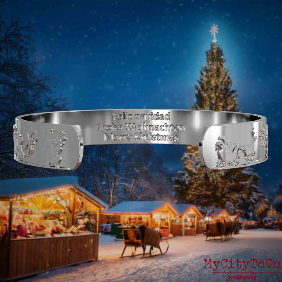 Innenseite eines silbernen Armreifs mit Reliefs weihnachtlicher Motive und der mehrsprachigen Gravur Frohe Weihnachten. Den Hintergrund bildet ein naechtliches Weihnachtsmotiv.