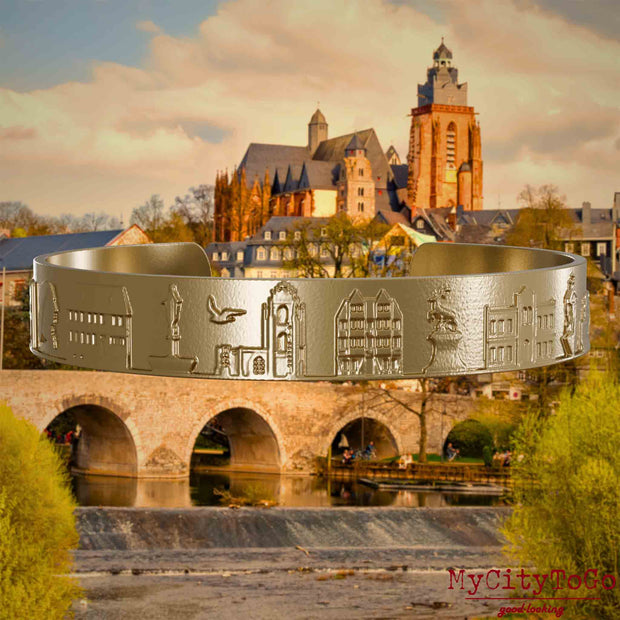 Armreif aus vergoldetem Edelstahl mit Reliefs bekannter Sehenswürdigkeiten der Stadt Wetzlar. Den Hintergrund bildet eine Ansicht der Stadt Wetzlar.