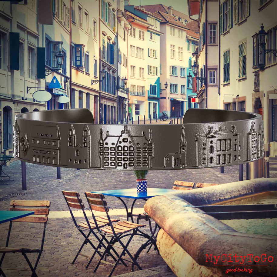 Armreif aus Titan mit Reliefs bekannter Sehenswürdigkeiten der Stadt Zuerich. Den Hintergrund bildet eine Ansicht der Stadt Zuerich.